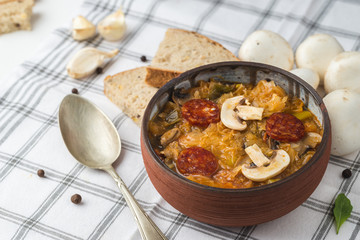 Slovak Christmas national cabbage soup in small black pot with sausage on the tablecloth background.