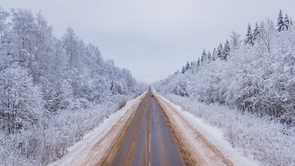 Aerial view of country road going through the beautiful snow covered landscapes.