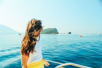 young pretty woman at boat nose sea with mountains and island on background