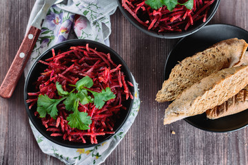 Thinly sliced ​​fresh beets in a black salad bowl with sprigs of cilantro ready for eating are on a wooden table. Shredded beet salad with toasts, closeup. Thinly shredded beet salad