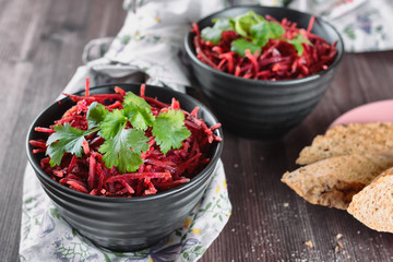 Thinly sliced ​​fresh beets in a black salad bowl with sprigs of cilantro ready for eating are...