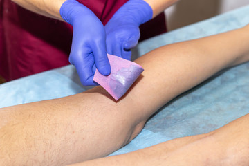 Beautician Waxing Leg Of Woman With Wax Strip At Beauty Clinic