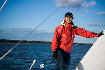 Young man skipper in red windbreaker and black cap sets the sails on a sailing yacht