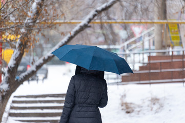 A woman with a black umbrella walking along a black and white landscape during snow