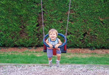 Cute happy smiling little child having fun riding on swing at children playground on summer day. Carefree childhood.