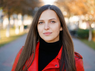 Outdoor headshot of 20s year stylish brunette woman in red leather coat on lunch break drinking coffee or tea to go. Autumn urban background.
