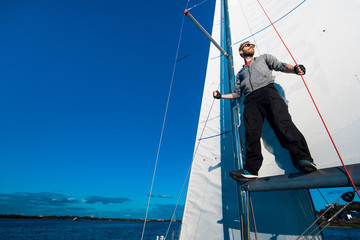 Fototapeta premium Young seaman on a sailboat standing on a sail boom. Captain of the yacht in the open sea.