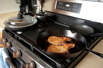 Pork chops frying in a cast iron pan on a stove top.