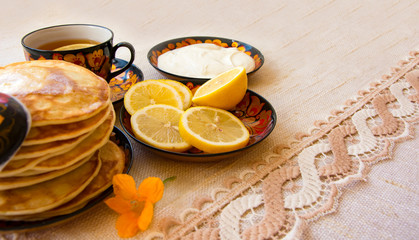 tea in a painted Cup, on a saucer sliced lemon, pancakes, sour cream and a wooden spoon for overlaying. tea party in rustic style