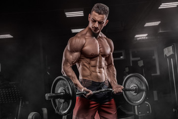 Young handsome sexy man, athlete, bodybuilder, weightlifter, in a modern gym is covered with a dark...