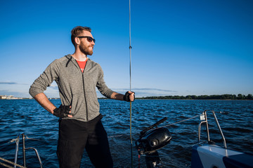 Obraz premium Young man on a catamaran standing and holding rope in front of a blue sky during cruising.