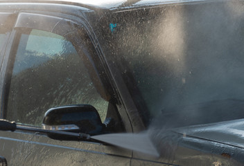 Spraying water from a high pressure hose to the side of a car at a self-service car wash