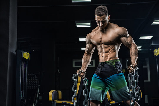 Young handsome sexy man, athlete, bodybuilder, weightlifter, in a modern gym is covered with a dark background, doing exercises for the biceps using sporting goods - weights. 