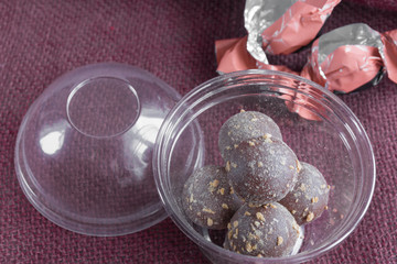 Closeup chocolate candies truffles in plastiс box on burgundy textile. Side view. Food photography concept