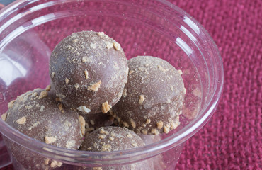Closeup chocolate candies truffles in plastiс box on burgundy textile. Side view. Food photography concept
