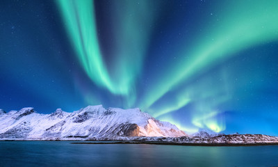 Aurora borealis auf den Lofoten, Norwegen. Grüne Nordlichter über Bergen und Ozeanufer. Nachtwinterlandschaft mit Aurora und Reflexion auf der Wasseroberfläche.