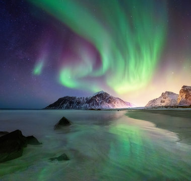 Aurora borealis on the Lofoten islands, Norway. Green northern lights above mountains and beach. Night sky with polar lights. Night winter landscape with aurora.