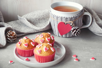 Muffins decorated with sugar hearts and a cup with red heart on light gray background