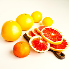 Citrus fruits - lemons, grapfruits, mandarins, oranges - on white tables.