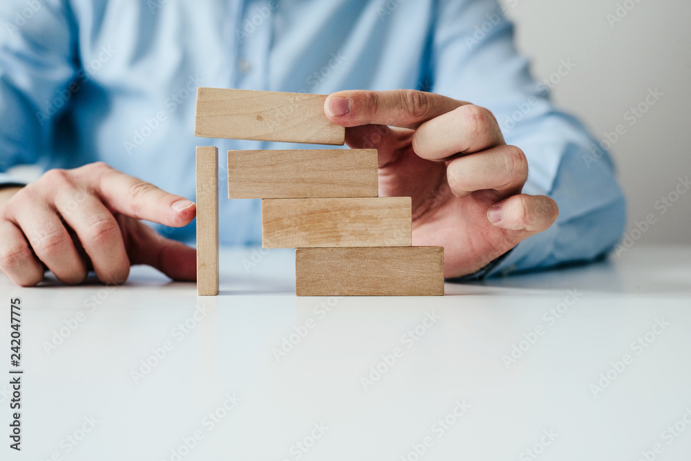 Wall mural Businessman in a blue shirt arranges wooden jigsaw blocks. The man arranges empty blocks one on top of the other. Different concepts to supplement with content. Business concept, HR.