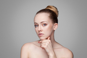 Beauty woman. Beautiful model with perfect fresh clean skin touch chin. Blonde brunette bun hair Youth and skin care concept. makeup and cosmetology. indoor studio shot, isolated on grey background.