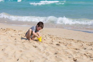 Little Kid playing with sand on the beach alone. Little boy near sea. Summer play.