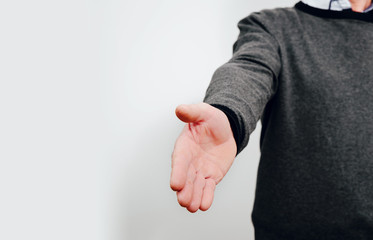 Holding out a hand in front of a man. A man wearing a gray sweater stretches out a helping hand, greeting or saying goodbye. Greetings concept.