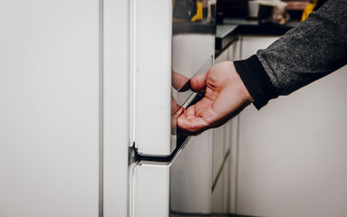 Opening the fridge, pulling out food. Preparing a meal from ingredients from the fridge. Taking care of food, storage in the fridge. The man is holding the white fridge behind the door.