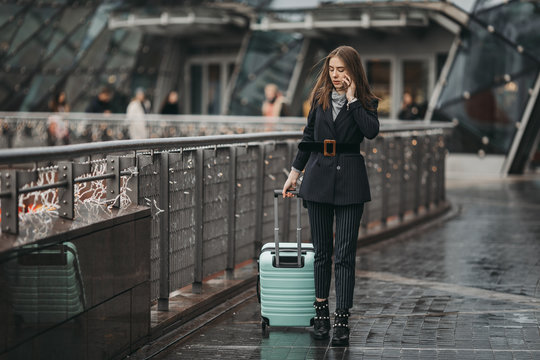 Businesswoman on airport talking on the smartphone while walking with hand luggage in train station or airpot going to boarding gate. Girl using mobile phone and watch for conversation. - Image