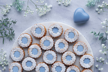 Obraz na płótnie Canvas Top view of flower Linzer cookies with blue glazing on light blue background decorated with white flowers and ceramic heart