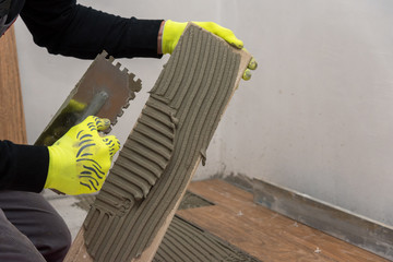 Worker placing ceramic floor tiles on adhesive surface.