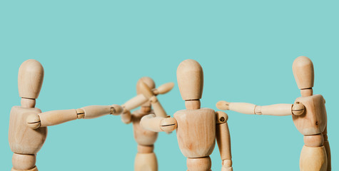 A wooden mannequin covers his face with his hands in front of others on a pastel background. Pointing finger at the victim. The concept of ridiculing, harassing people. Discrimination and problems.
