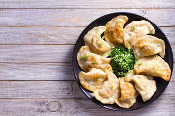 Fried dumplings stuffed with meat and served with chopped parsley and spring onion on a black plate on a wooden rustic table. View from above, top studio shot