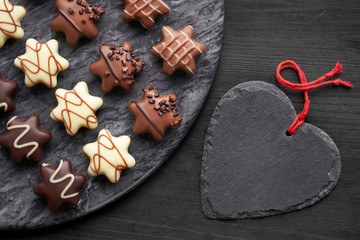 Star-shaped chocolates on dark grey stone board with black heart on dark background