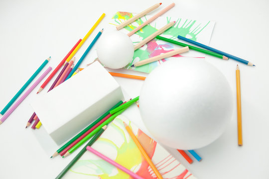 esferas y prisma blancos con pinturas abstractas y l&aacute;pices de colores desordenados sobre fondo blanco