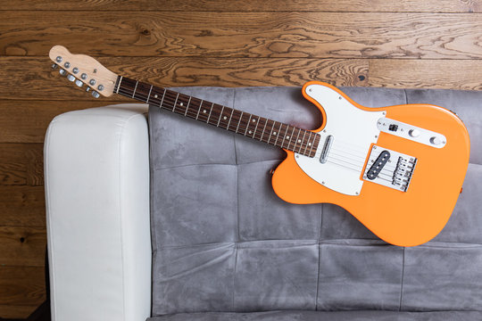 Orange electric guitar on a leather sofa top view, wooden floor