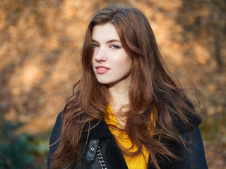 Fabulous redhead woman with long hair in yellow sweater black leather jacket on blurred autumn background.