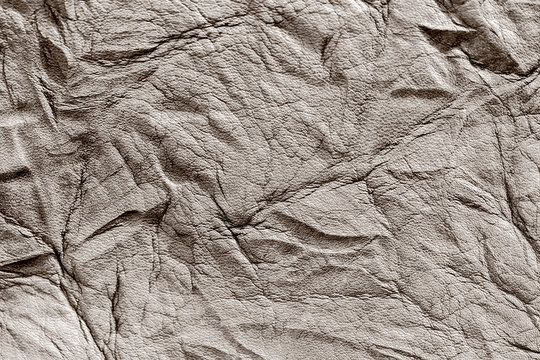 Texture of rough crumpled genuine leather close-up, with embossed wrinkles, matte surface, trendy background