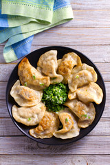 Fried dumplings stuffed with meat and served with chopped parsley and spring onion on a black plate on a wooden rustic table. View from above, top studio shot