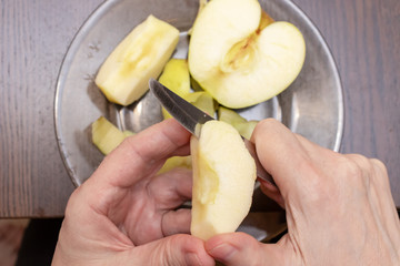 Female hands peeling skin off of a yellow apple with a knife