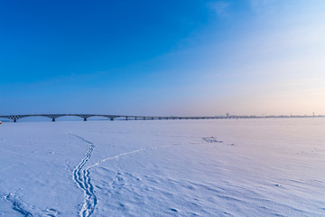 Sunset on the Volga in winter. Footprints in the snow and the Saratov Bridge
