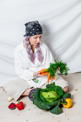 Beautiful caucasian vegan woman with vegetables sitting on a flooor. Spring time concept and healthy meal