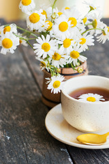 Obraz na płótnie Canvas cup of herbal chamomile tea with fresh daisy flowers on wooden background 