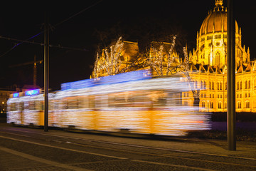 Festively decorated light tram ,Fenyvillamos, on the move with Parliament of Hungary at Kossuth square by night. Christmas season in Budapest, Hungary