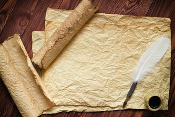 paper scroll with feather pen and ink pot on wood background
