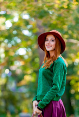 Young redhead woman with bag and hat in autumn park outdoor