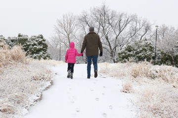 Father and daughter walking up a snowy hill holding hands