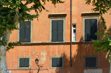A set of apartments, covered with traditional ochre-coloured paint, in Venice, Italy. The windows have black shutters, and the paint is peeling. A black lamp is attached to the wall,.