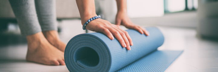 Yoga zu Hause aktiver Lebensstil Frau rollende Übungsmatte im Wohnzimmer für morgendliche Meditation Yoga-Banner-Hintergrund.