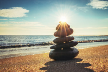 Stones balance on the beach sand. Sunrise over the sea. Zen meditation and yoga practices.